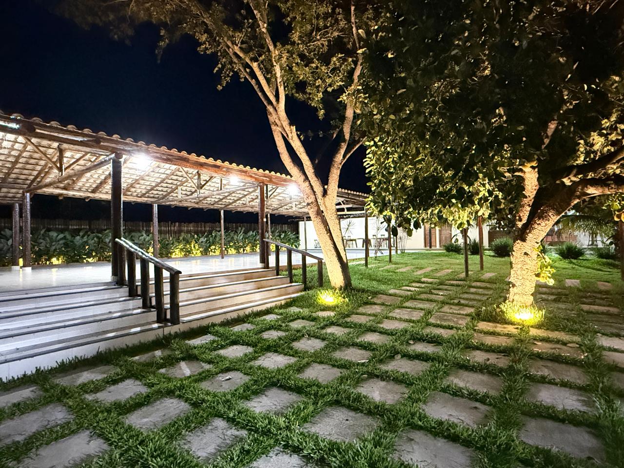 Jardim iluminado à noite, com escadaria e quiosque ao fundo