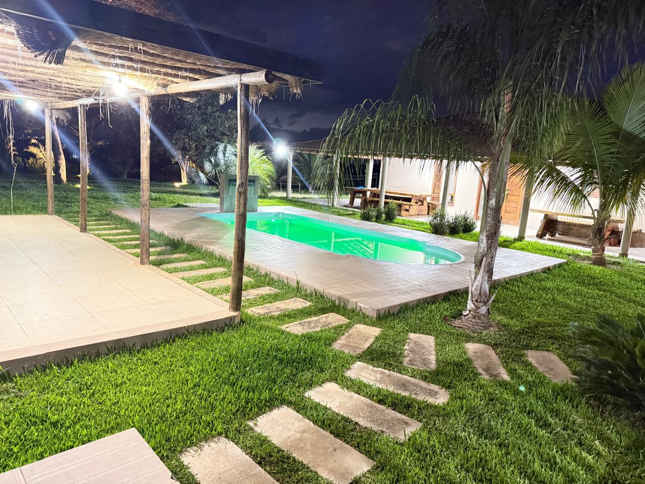 Piscina iluminada à noite, com caminho de pedras no gramado